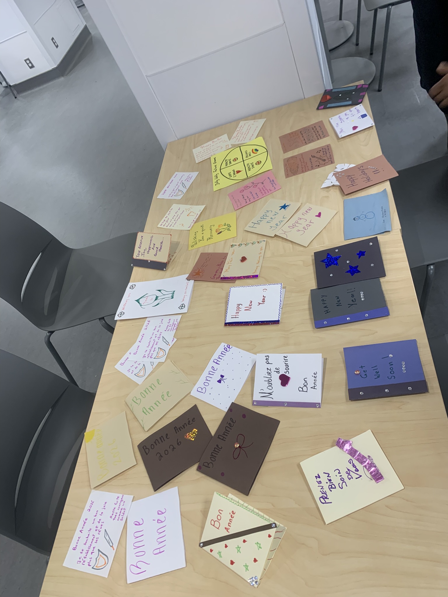 Table filled with finished cards showing messages like 'Bonne Année 2026' and 'Wishing you Well'
